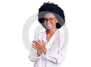 Young african american woman wearing doctor coat and stethoscope clapping and applauding happy and joyful, smiling proud hands