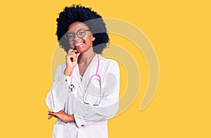 Young african american woman wearing doctor coat and stethoscope looking confident at the camera smiling with crossed arms and