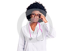 Young african american woman wearing doctor coat and stethoscope worried and stressed about a problem with hand on forehead,