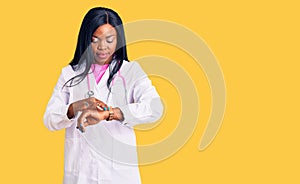 Young african american woman wearing doctor stethoscope checking the time on wrist watch, relaxed and confident