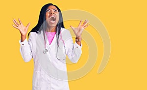 Young african american woman wearing doctor stethoscope crazy and mad shouting and yelling with aggressive expression and arms