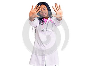 Young african american woman wearing doctor stethoscope doing frame using hands palms and fingers, camera perspective