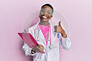 Young african american woman wearing doctor stethoscope holding clipboard smiling happy and positive, thumb up doing excellent and