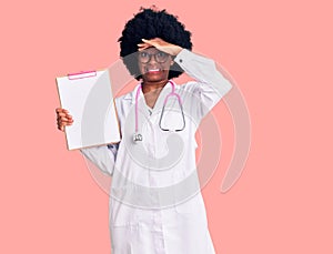 Young african american woman wearing doctor stethoscope holding clipboard stressed and frustrated with hand on head, surprised and