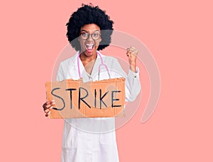 Young african american woman wearing doctor stethoscope holding strike banner screaming proud, celebrating victory and success