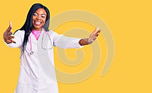 Young african american woman wearing doctor stethoscope looking at the camera smiling with open arms for hug