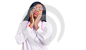 Young african american woman wearing doctor stethoscope tired hands covering face, depression and sadness, upset and irritated for