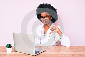 Young african american woman wearing doctor stethoscope working using computer laptop with angry face, negative sign showing