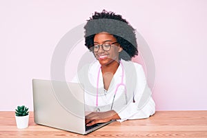 Young african american woman wearing doctor stethoscope working using computer laptop looking positive and happy standing and