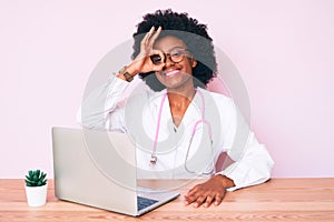 Young african american woman wearing doctor stethoscope working using computer laptop smiling happy doing ok sign with hand on eye