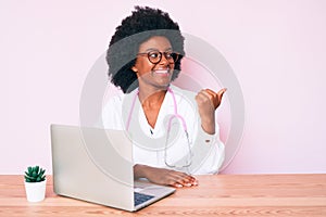 Young african american woman wearing doctor stethoscope working using computer laptop smiling with happy face looking and pointing
