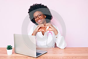 Young african american woman wearing doctor stethoscope working using computer laptop smiling in love showing heart symbol and