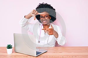 Young african american woman wearing doctor stethoscope working using computer laptop smiling making frame with hands and fingers