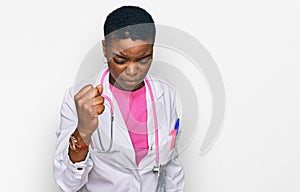 Young african american woman wearing doctor uniform and stethoscope angry and mad raising fist frustrated and furious while