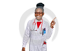 Young african american woman wearing doctor uniform and stethoscope with a big smile on face, pointing with hand finger to the