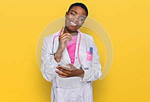 Young african american woman wearing doctor uniform and stethoscope with a big smile on face, pointing with hand and finger to the