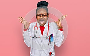 Young african american woman wearing doctor uniform and stethoscope celebrating mad and crazy for success with arms raised and