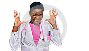 Young african american woman wearing doctor uniform and stethoscope celebrating mad and crazy for success with arms raised and