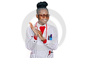 Young african american woman wearing doctor uniform and stethoscope clapping and applauding happy and joyful, smiling proud hands