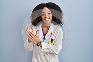 Young african american woman wearing doctor uniform and stethoscope clapping and applauding happy and joyful, smiling proud hands