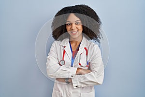 Young african american woman wearing doctor uniform and stethoscope happy face smiling with crossed arms looking at the camera