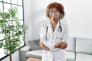 Young african american woman wearing doctor uniform and stethoscope happy face smiling with crossed arms looking at the camera
