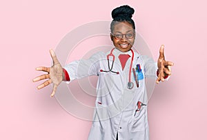 Young african american woman wearing doctor uniform and stethoscope looking at the camera smiling with open arms for hug