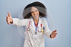 Young african american woman wearing doctor uniform and stethoscope looking at the camera smiling with open arms for hug
