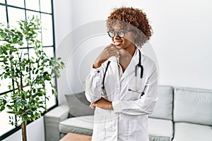 Young african american woman wearing doctor uniform and stethoscope looking confident at the camera smiling with crossed arms and