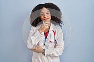 Young african american woman wearing doctor uniform and stethoscope looking confident at the camera smiling with crossed arms and