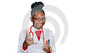 Young african american woman wearing doctor uniform and stethoscope pointing fingers to camera with happy and funny face