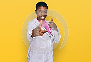 Young african american woman wearing doctor uniform and stethoscope pointing fingers to camera with happy and funny face