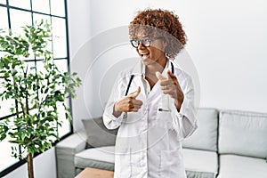 Young african american woman wearing doctor uniform and stethoscope pointing fingers to camera with happy and funny face