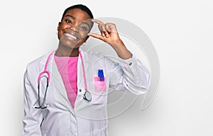 Young african american woman wearing doctor uniform and stethoscope smiling and confident gesturing with hand doing small size
