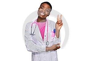 Young african american woman wearing doctor uniform and stethoscope smiling with happy face winking at the camera doing victory