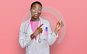 Young african american woman wearing doctor uniform and stethoscope smiling and looking at the camera pointing with two hands and