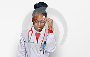 Young african american woman wearing doctor uniform and stethoscope worried and stressed about a problem with hand on forehead,