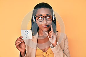 Young african american woman wearing operator headset holding question mark serious face thinking about question with hand on
