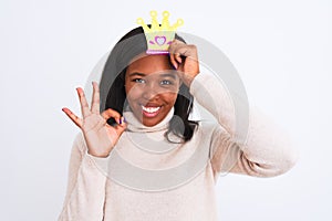 Young african american woman wearing pretend queen crown over isolated background doing ok sign with fingers, excellent symbol