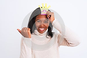 Young african american woman wearing pretend queen crown over isolated background pointing and showing with thumb up to the side