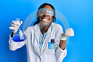 Young african american woman wearing scientist uniform holding test tube screaming proud, celebrating victory and success very