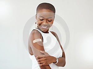 Young African American woman wearing and showing a bandaid on her arm standing against a white studio background. Happy