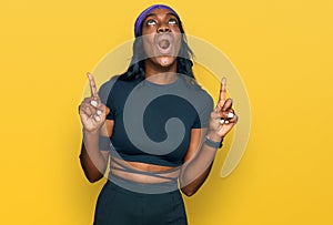 Young african american woman wearing sportswear amazed and surprised looking up and pointing with fingers and raised arms