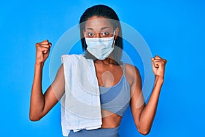 Young african american woman wearing sportswear and medical mask screaming proud, celebrating victory and success very excited