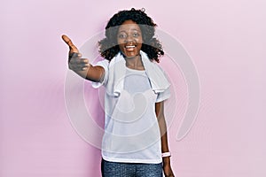 Young african american woman wearing sportswear and towel smiling friendly offering handshake as greeting and welcoming