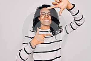 Young african american woman wearing striped sweater and glasses over white background smiling making frame with hands and fingers