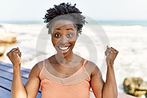 Young african american woman wearing summer clothes standing at the beach screaming proud, celebrating victory and success very