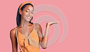Young african american woman wearing summer outfit smiling cheerful presenting and pointing with palm of hand looking at the