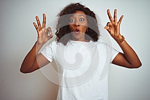 Young african american woman wearing t-shirt standing over isolated white background looking surprised and shocked doing ok