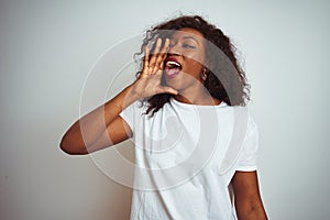 Young african american woman wearing t-shirt standing over isolated white background shouting and screaming loud to side with hand